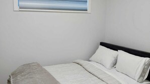 A bedroom with a bed, pillows, a blanket, and a window with horizontal blinds.