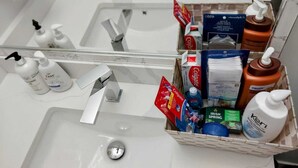 A bathroom sink with a mirror, a toothbrush holder, and a basket containing toiletries like toothpaste, shampoo, and soap.