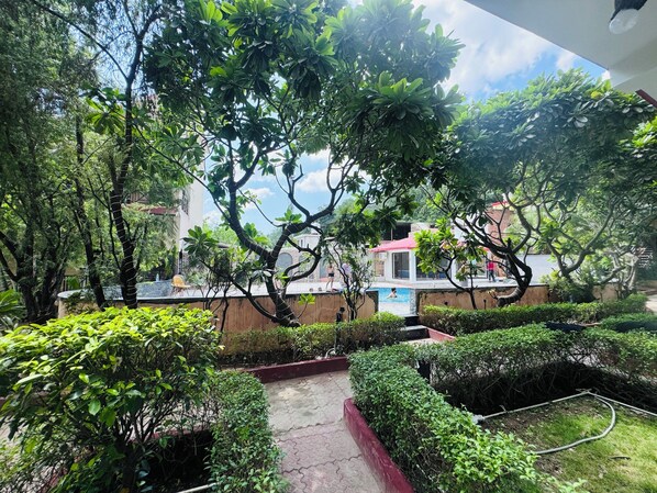 A lush garden with a swimming pool, surrounded by various plants and trees. - Staybook The Rudveda Resort (Ramnagar)