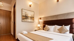 A hotel room with a large bed, a wooden door, a painting on the wall, and two wall sconces. - Staybook The Rudveda Resort (Ramnagar)