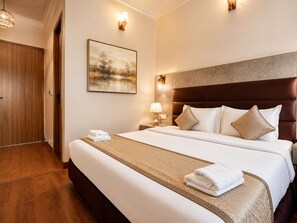 A hotel room with a large bed, a wooden door, a painting on the wall, and two wall sconces. - Staybook The Rudveda Resort (Ramnagar)