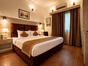 A hotel room with a large bed, two bedside tables with lamps, a wall-mounted air conditioner, and a window with curtains. - Staybook The Rudveda Resort (Ramnagar)