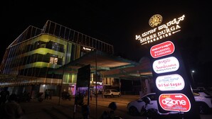 Un immeuble à plusieurs étages, doté d’une enseigne lumineuse indiquant les différents services qu’il propose, notamment une salle de réception pour mariages, un restaurant et un service de stationnement.