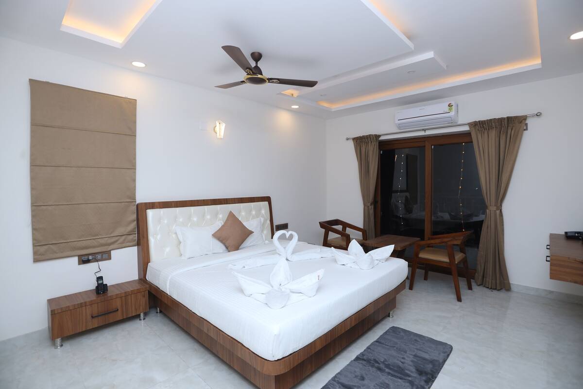 A modern hotel room with a large bed, a desk, a chair, a ceiling fan, and an air conditioning unit.