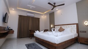 Une chambre d’hôtel moderne dotée d’un grand lit, d’un ventilateur de plafond, d’un téléviseur à écran plat et d’une table de chevet en bois.