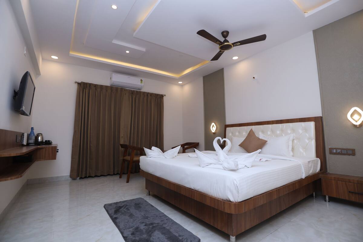A modern hotel room with a large bed, a ceiling fan, a flat-screen TV, and a wooden nightstand.