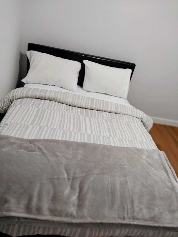 Uma cama com cabeceira preta, almofadas brancas e edredom listrado.