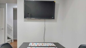 Un salón de conferencias con una larga mesa, sillas negras, un televisor montado y un cable fijado a la pared.