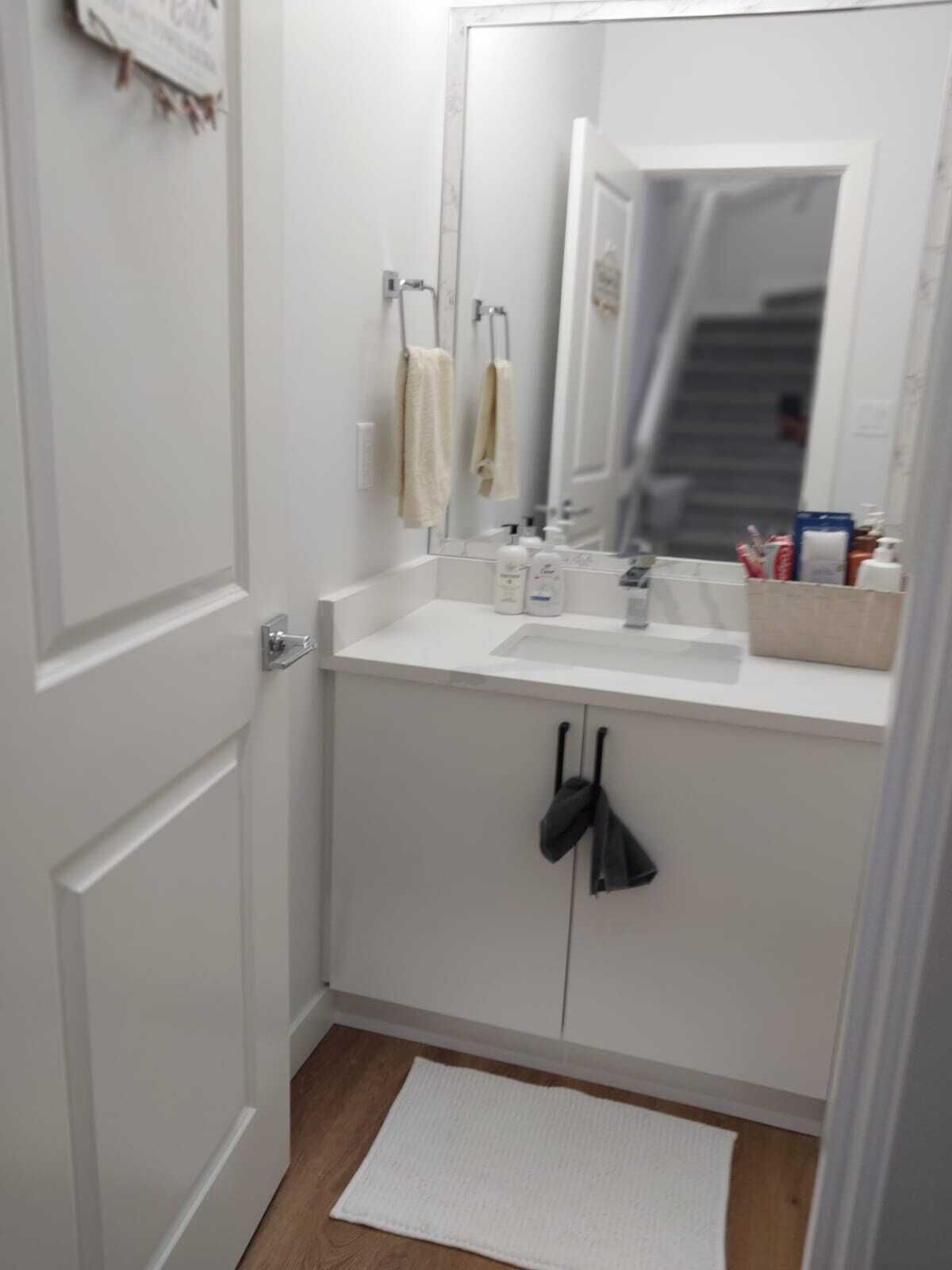A small, white bathroom with a single sink, a mirror, and a towel rack.