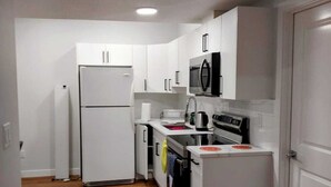 Una cocina compacta con armarios blancos, un microondas integrado, un refrigerador y un horno.