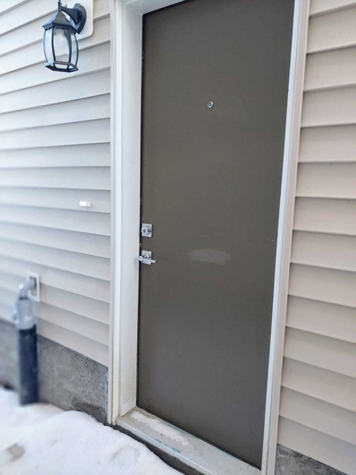 A closed door with a metal handle and a peephole, set in a white-framed window with horizontal siding.