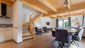 Amplia sala de estar con una escalera de madera, una mesa de comedor con sillas y una cocina con armarios y un televisor.