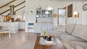 Ein großzügiger Wohnbereich mit Couch, Holz-Couchtisch und einer Küche im Hintergrund.
