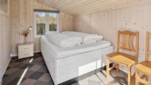 Ein Schlafzimmer mit einem Bett, Holzwänden, einem Fenster, einem Nachttisch und einem Sessel.