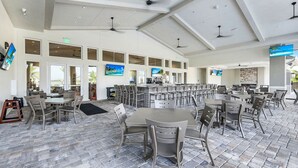 A spacious indoor dining area with multiple tables and chairs, large windows, ceiling fans, and a stone-tiled floor. - New Home in Paradise! (Fort Myers)