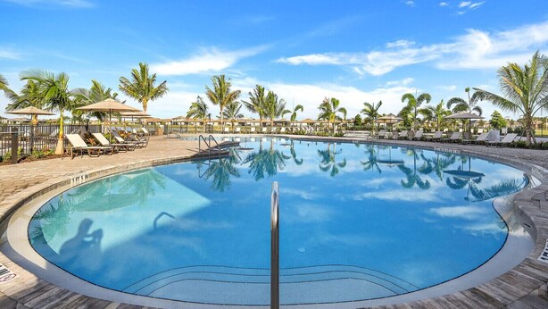 A circular pool with lounge chairs and palm trees around it. - New Home in Paradise! (Fort Myers)