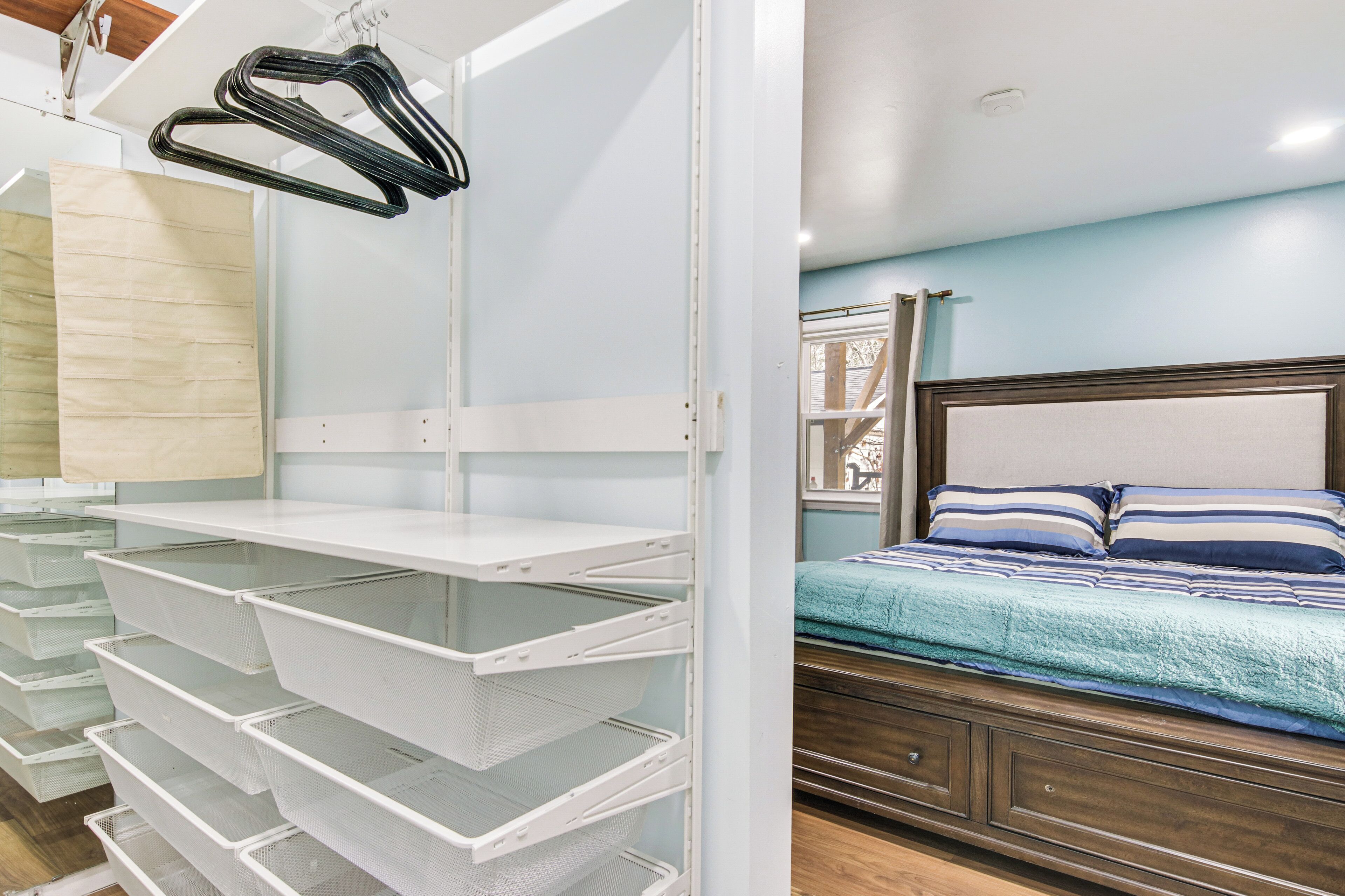 A bedroom with a bed, a nightstand, and a white shelving unit with baskets.