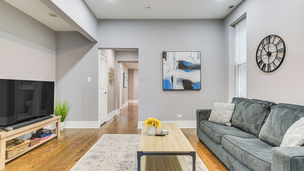 A modern living room with a flat-screen TV, grey sofa, and a coffee table with a vase of sunflowers. - 5 Mi to Dtwn: Ukrainian Village Apartment! (Chicago)