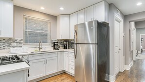 A modern kitchen with white cabinets, a stainless steel refrigerator, a gas stove, and a window with blinds. - 5 Mi to Dtwn: Ukrainian Village Apartment! (Chicago)
