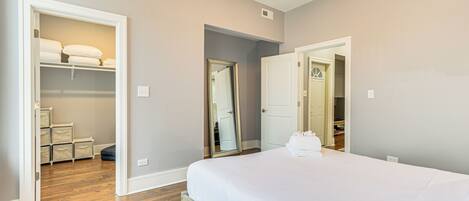 A bedroom with a large bed, a walk-in closet, and a mirror.