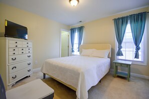Ein Schlafzimmer mit einem Bett, einer Kommode, einem Fernseher auf der Kommode und einem Fenster mit Vorhängen.