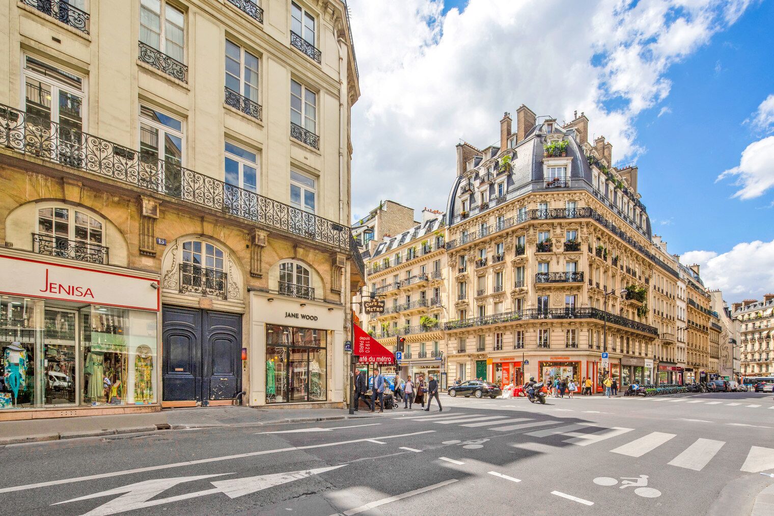 Une vue de rue avec un café appelé « JANE WOOD » et un magasin appelé « JENISA ».