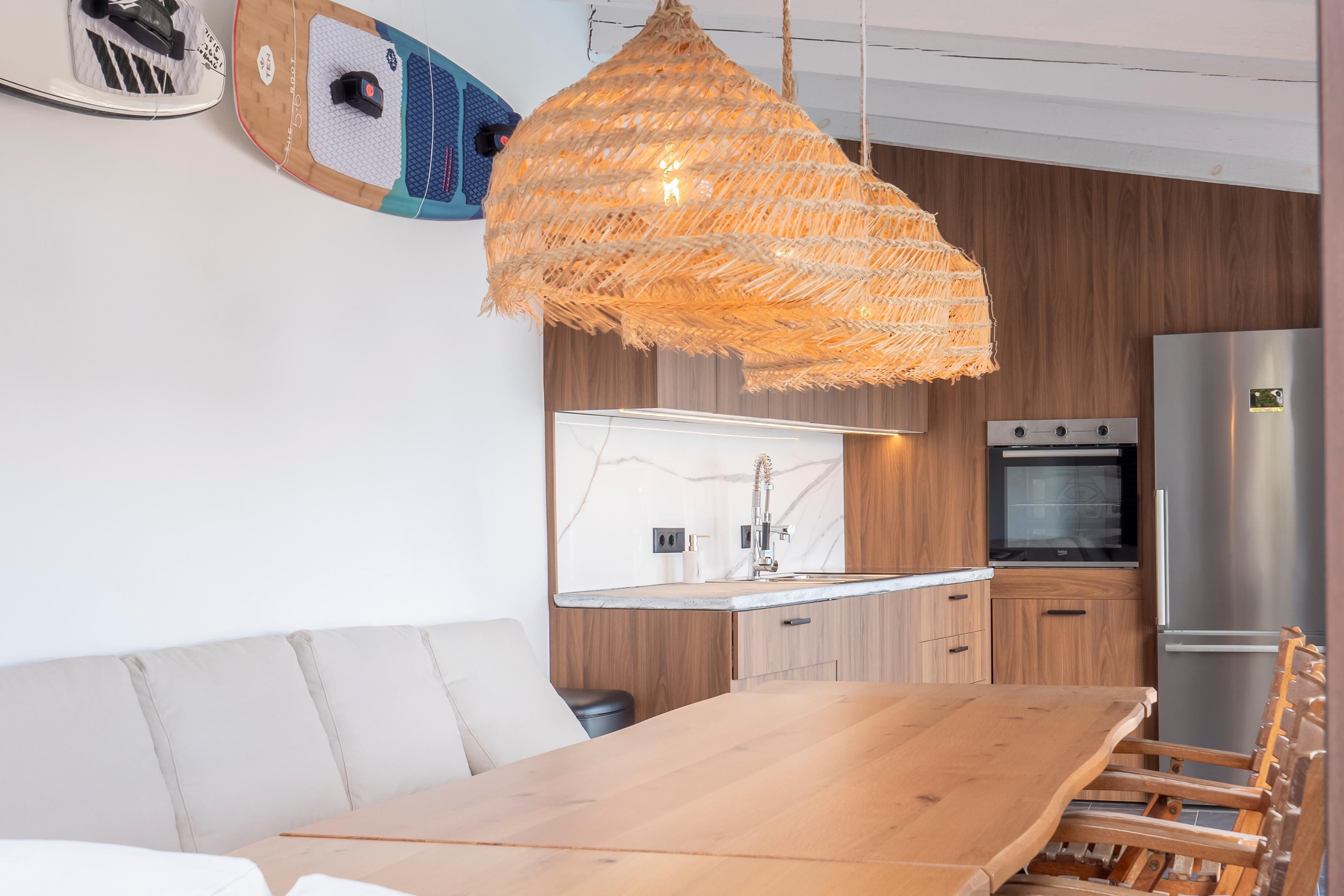 Een moderne keuken met houten kastjes, een roestvrijstalen koelkast en een hangende rotanlamp.