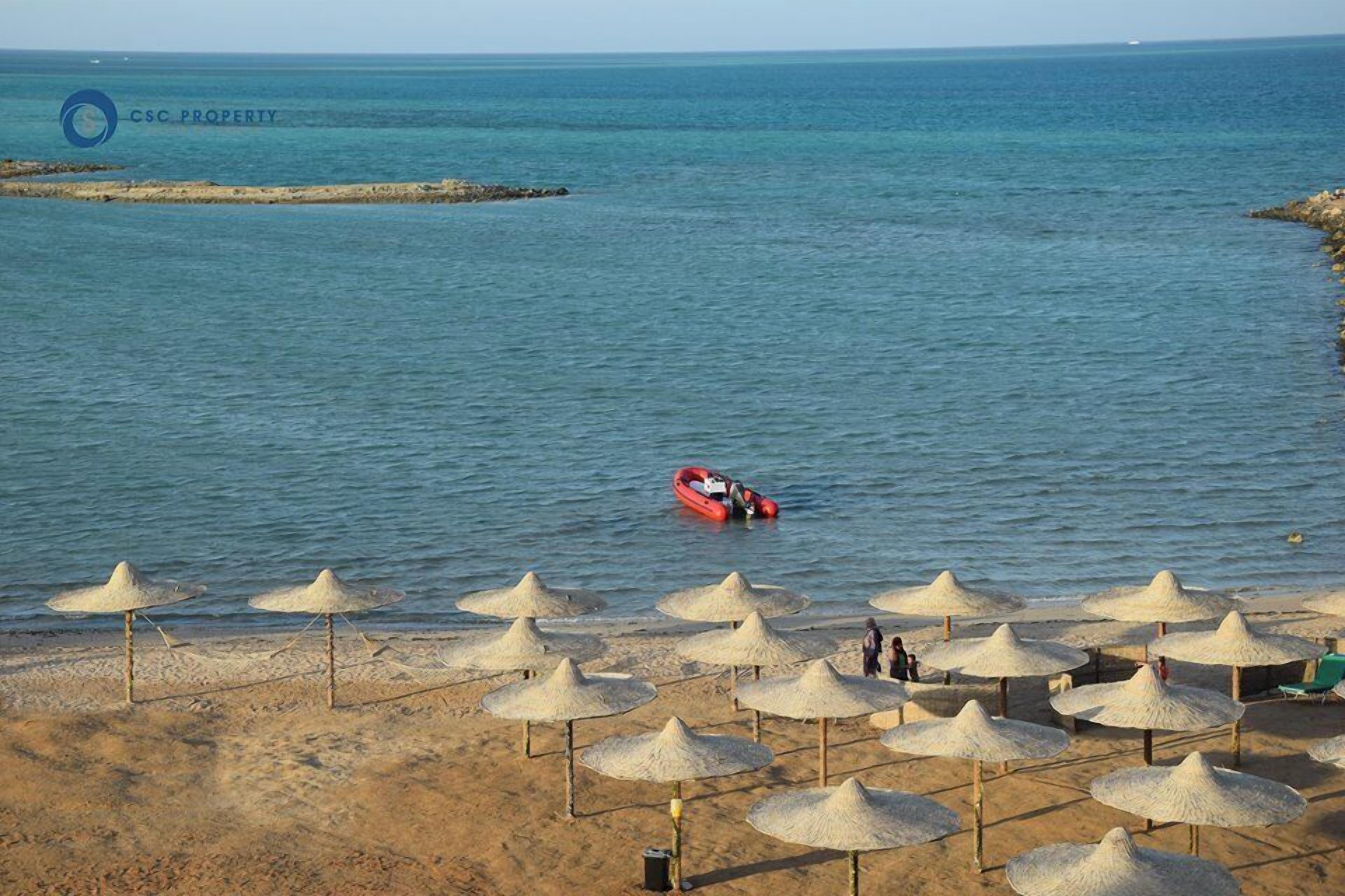 Een strand met parasols en een boot in het water.