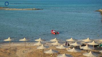 Een strand met parasols en een boot in het water.