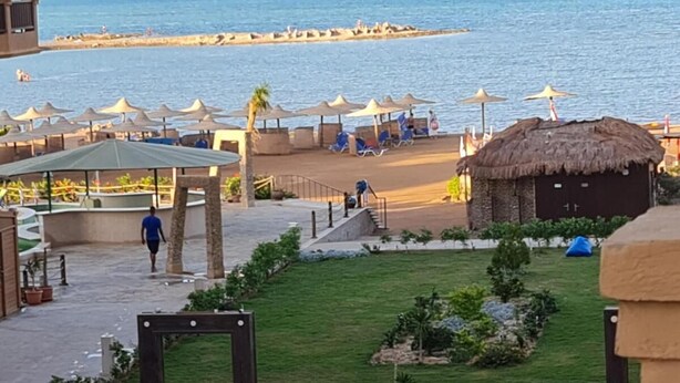 Ett semesterhotell vid stranden med en pool, parasoller och solstolar.
