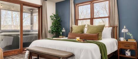 A bedroom with a large bed, a bench, a nightstand, a lamp, and a window with curtains.