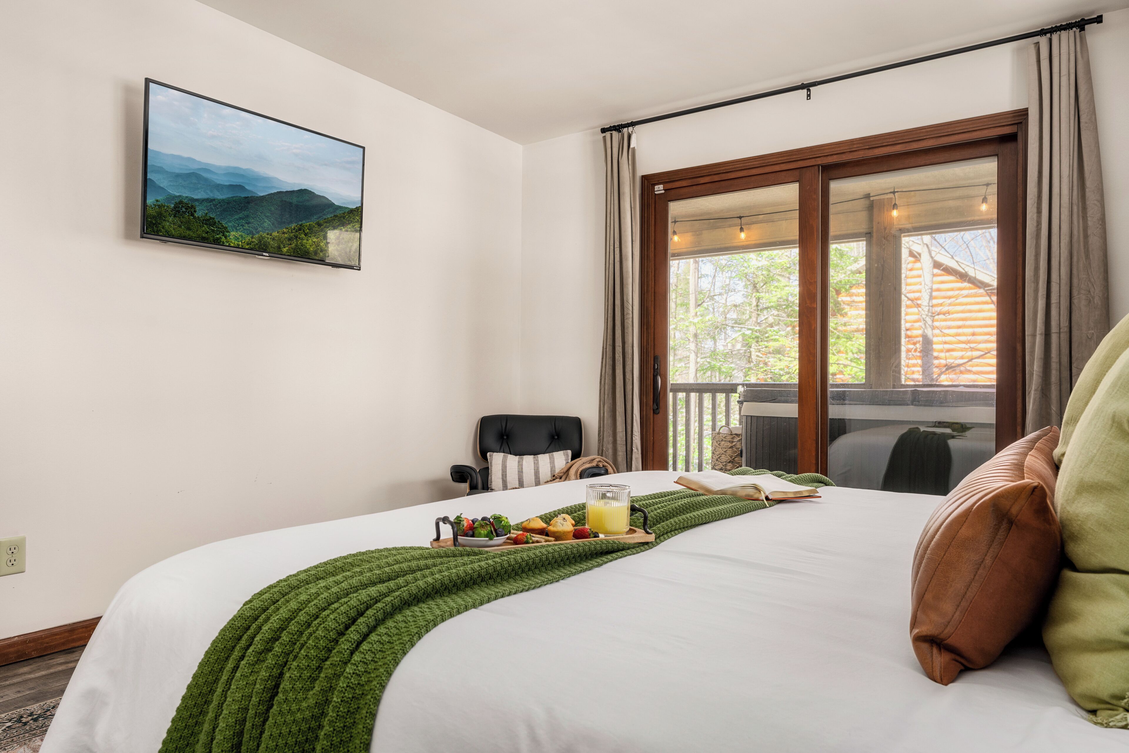 Habitación de hotel con cama, bandeja de desayuno, una silla, ventana con vista a árboles y un cuadro en la pared.