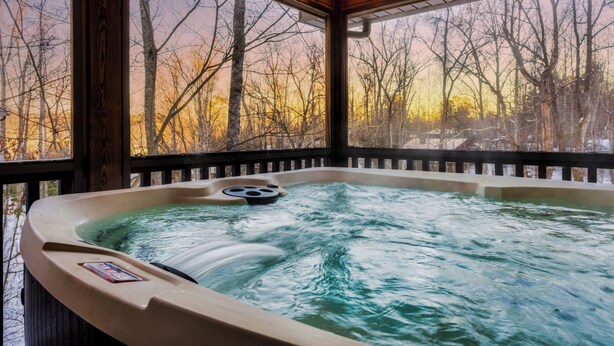 A hot tub with a view of leafless trees and a sunset.