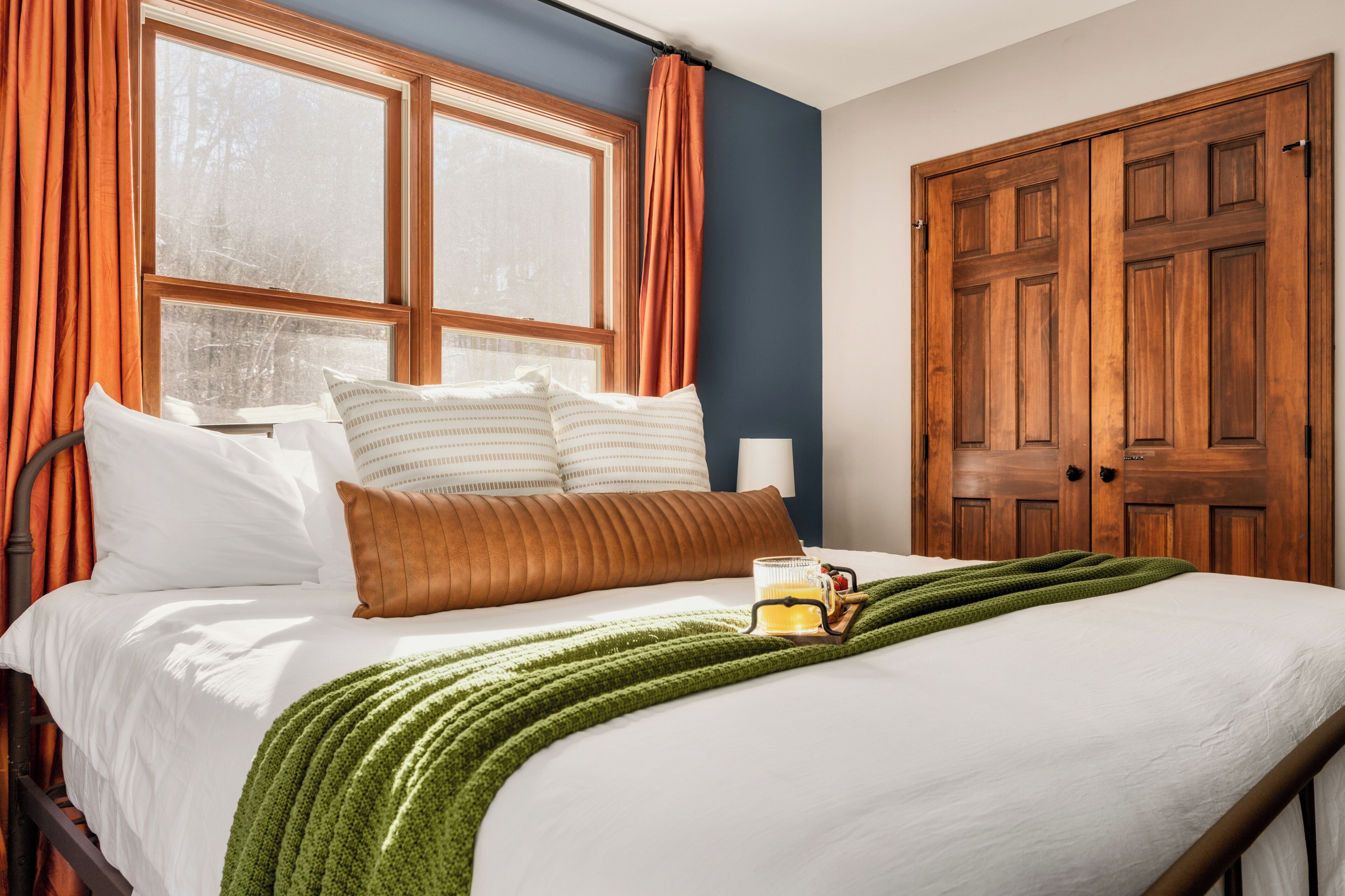 A neatly made bed with pillows, a green blanket, and a mug on it.
