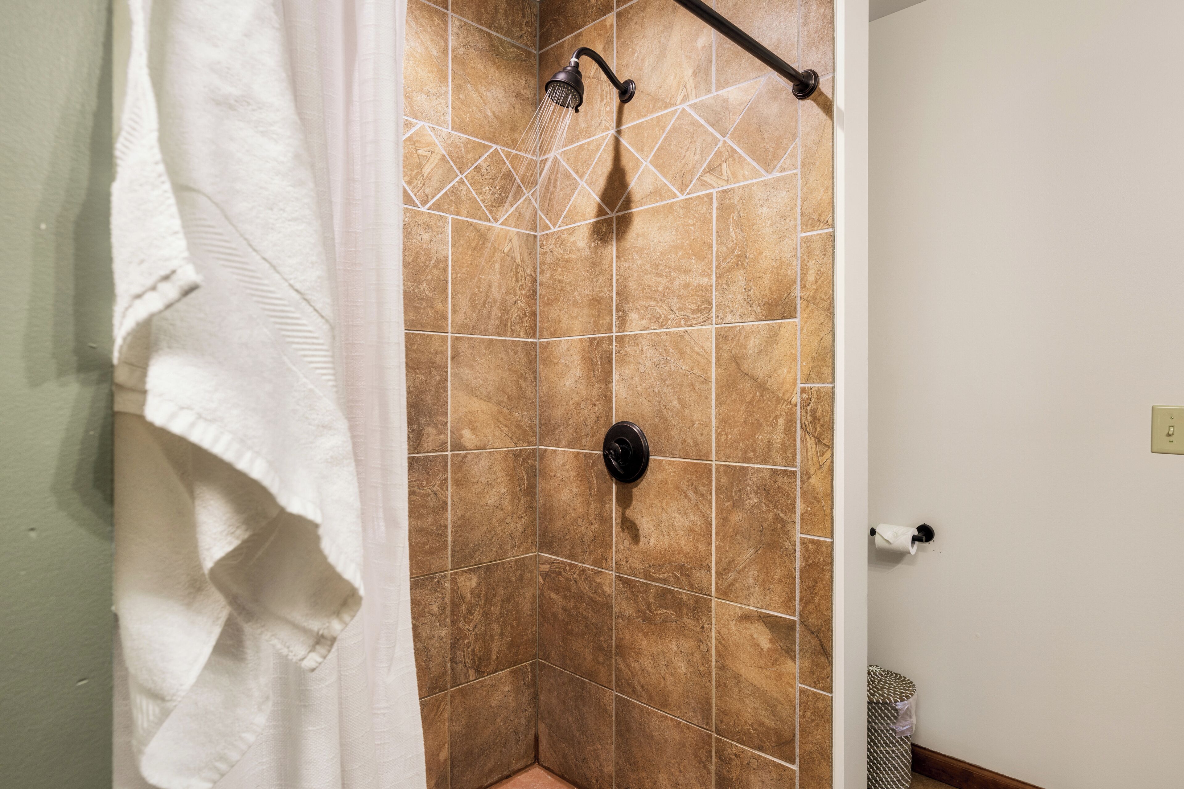 A shower with a rain showerhead, a towel rack, and a trash can.
