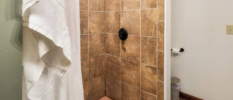 A shower with a rain showerhead, a towel rack, and a trash can.