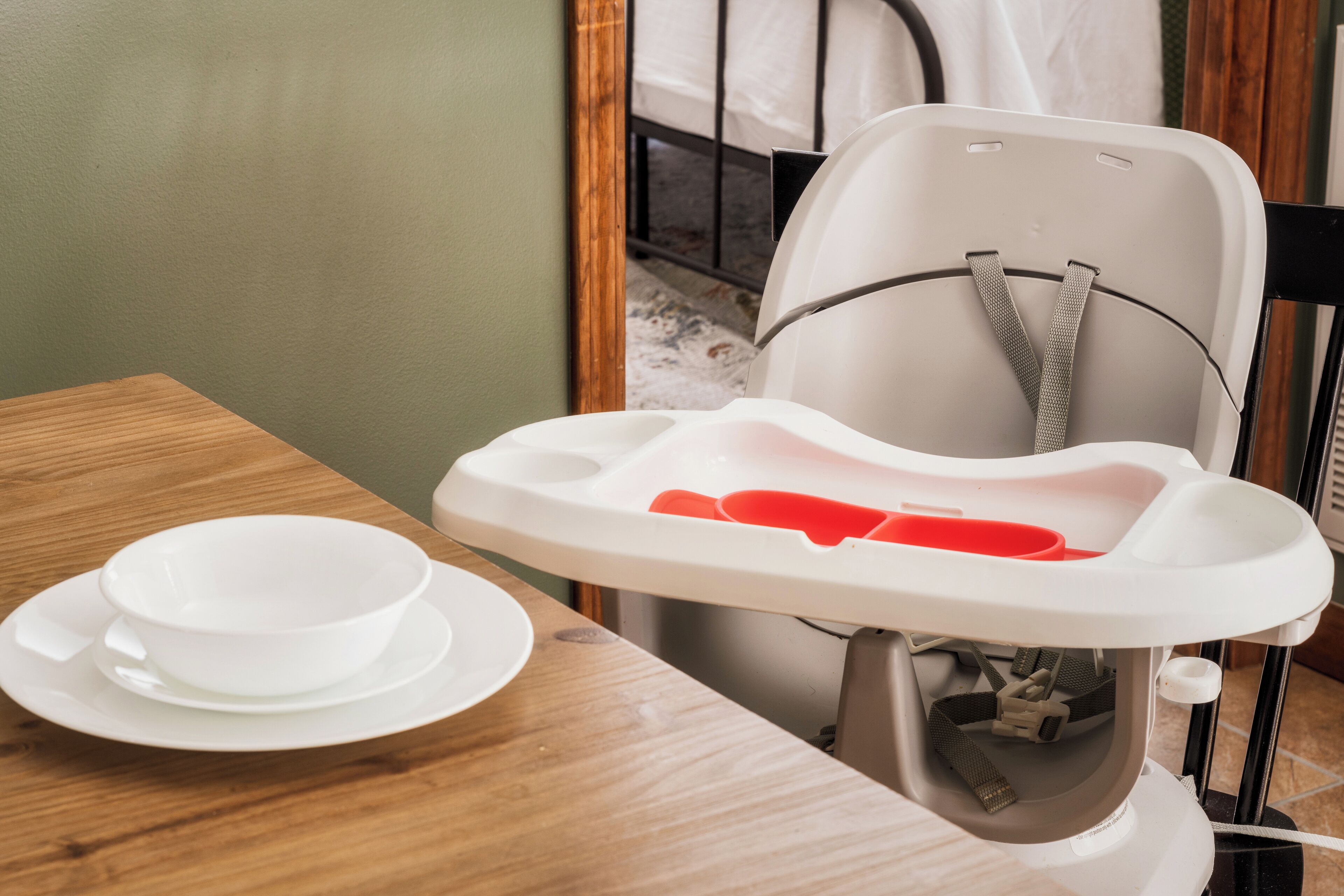 Una silla alta con mesita, un tazón blanco y un platillo sobre una mesa de madera.