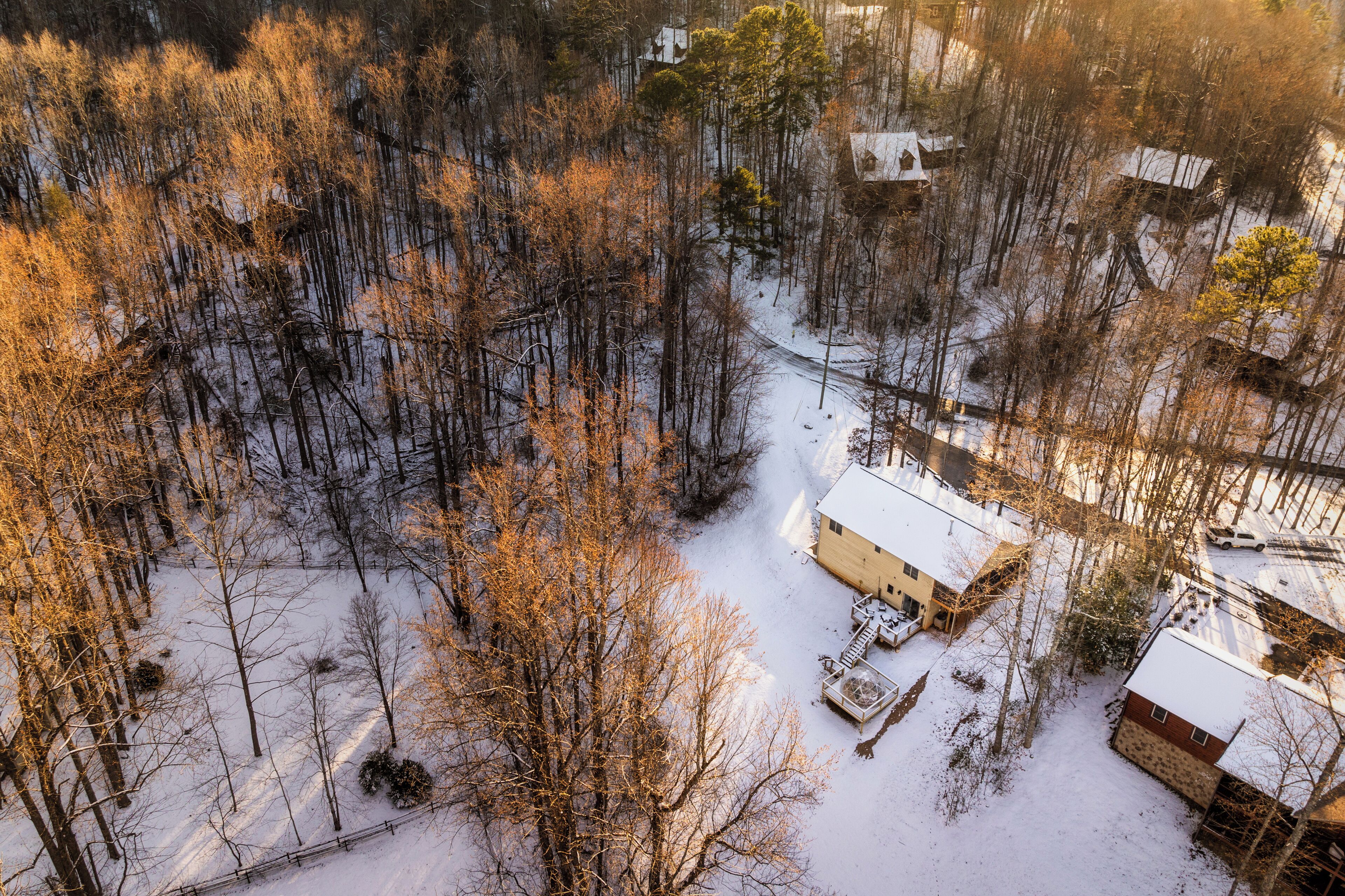 A snow-covered landscape with several buildings, including a house with a white roof and a shed.