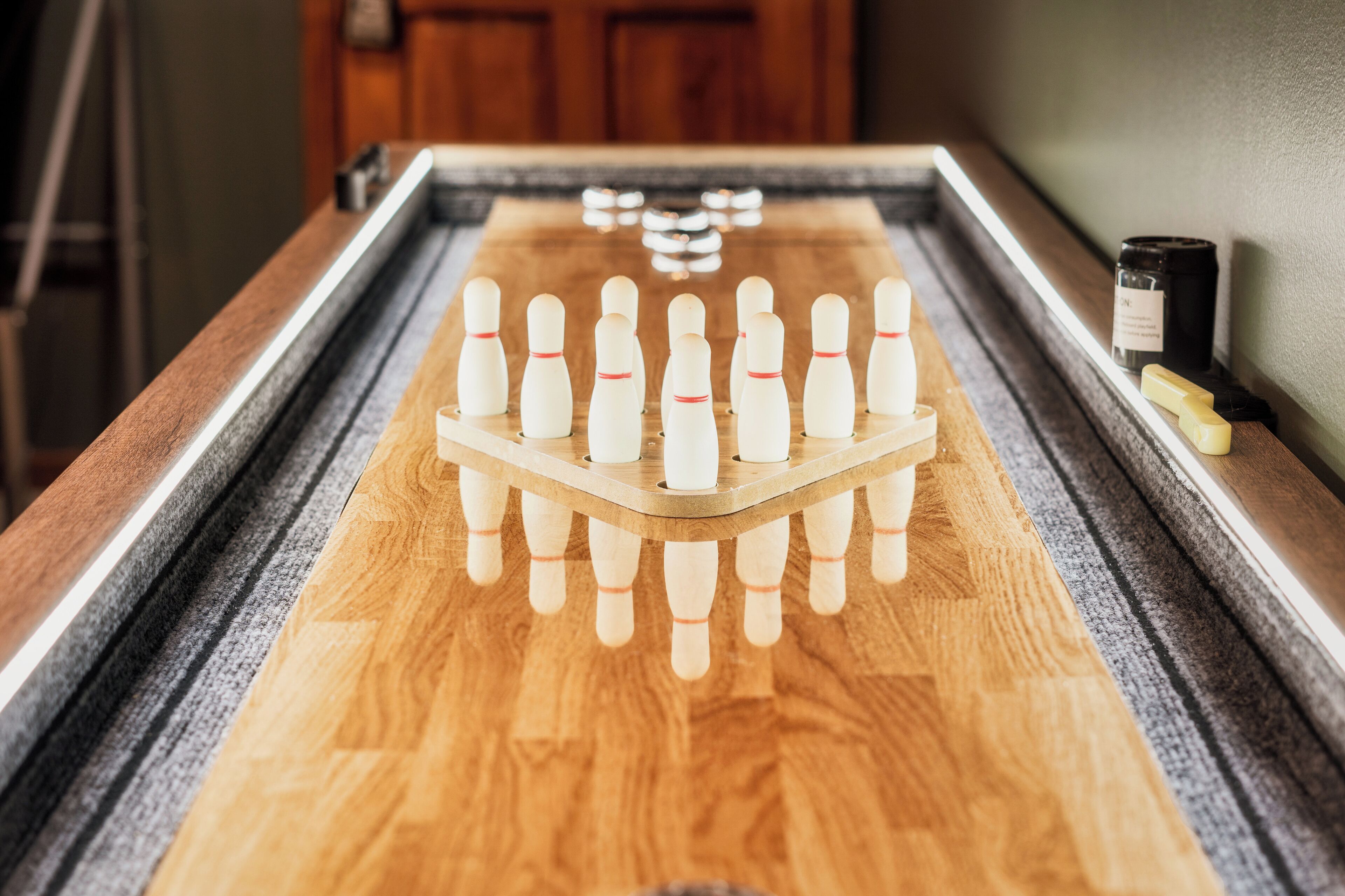 A wooden bowling alley with a set of pins and a candle on the side.
