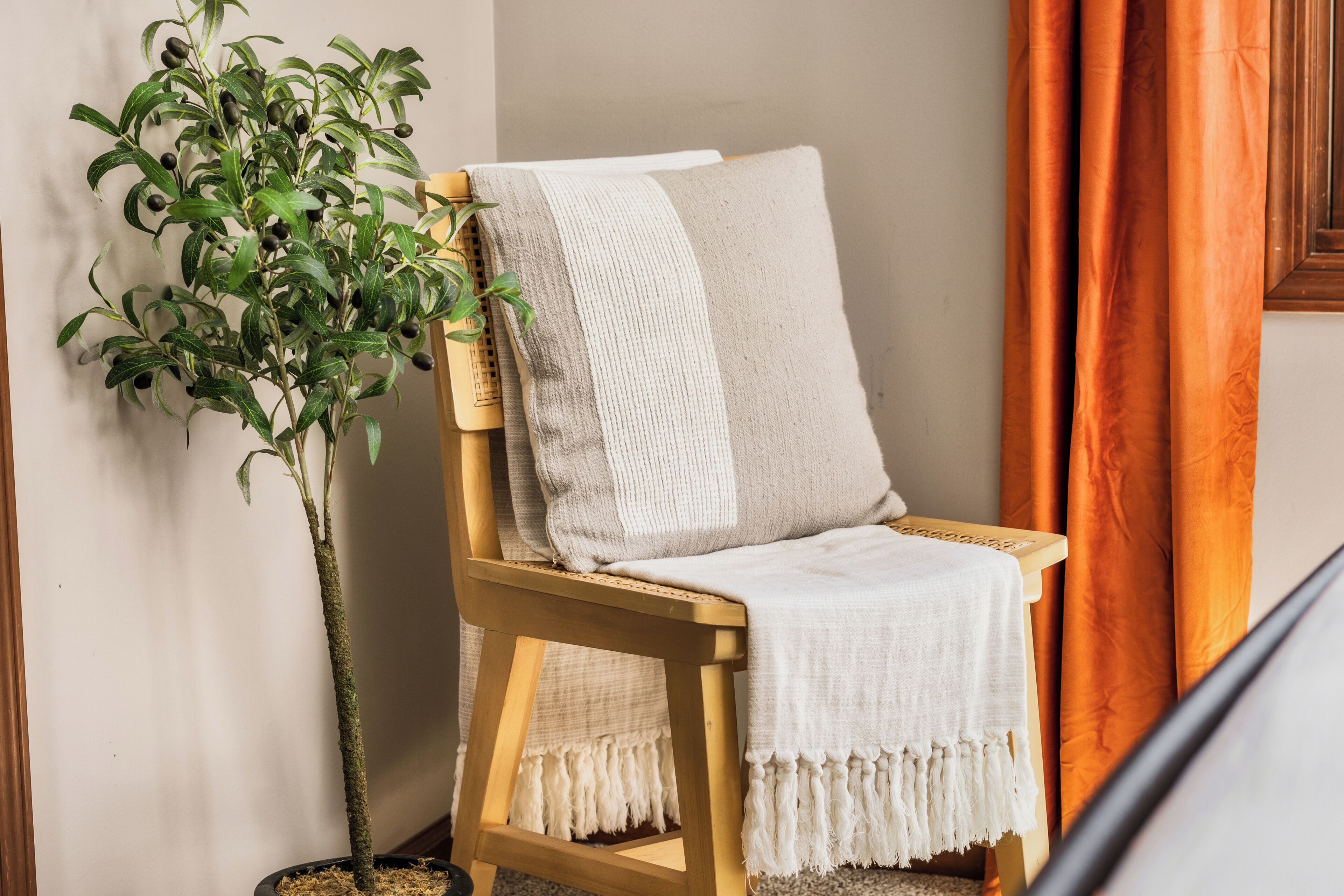 A wooden chair with a white throw blanket, a potted plant, and orange curtains.