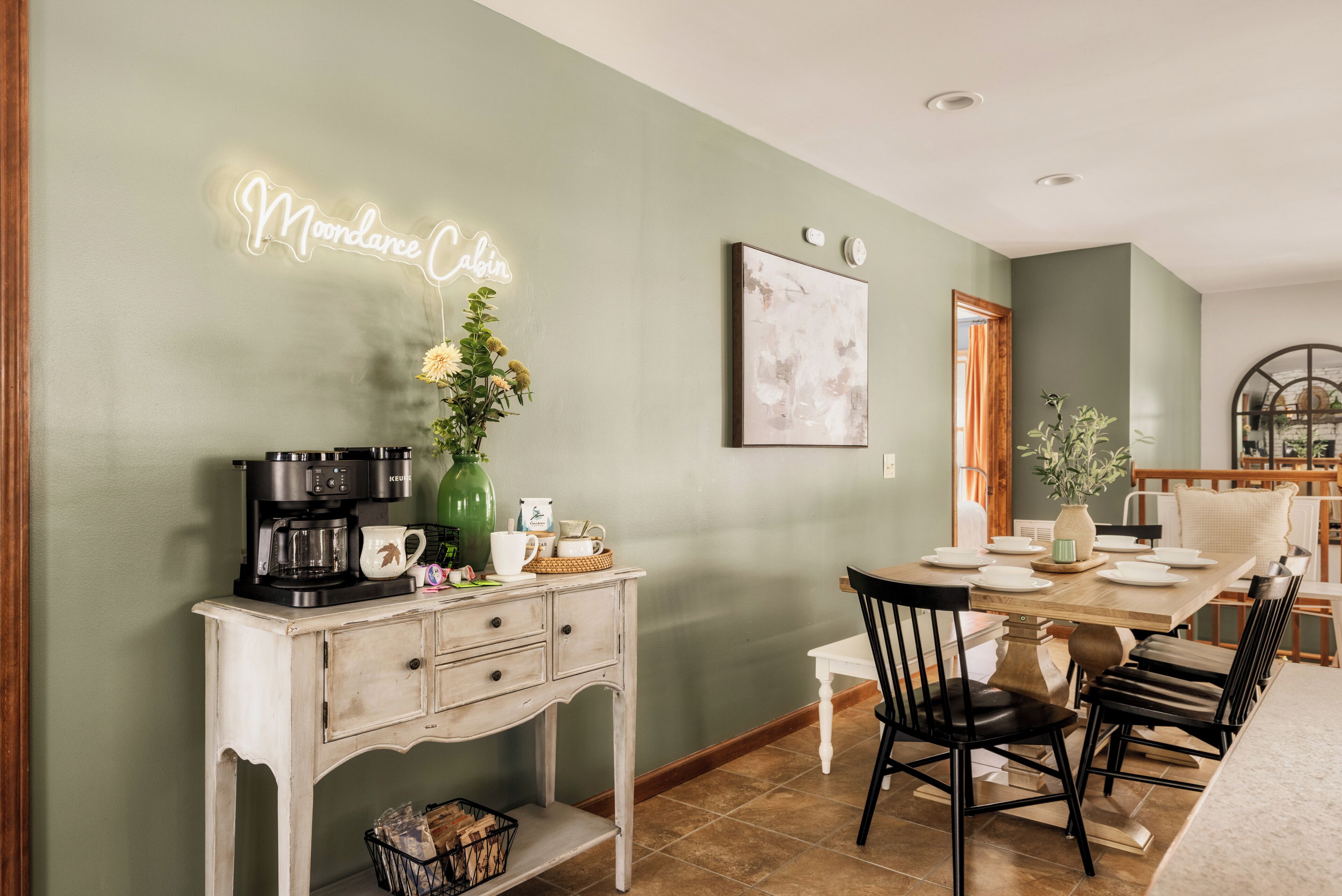 Un comedor con una señal de neón, una estación de café y una mesa de comedor preparada para cuatro comensales.