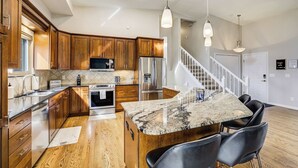 A modern kitchen with wooden cabinets, a granite island, and a stainless steel refrigerator.