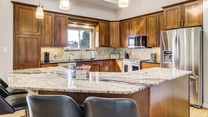 A modern kitchen with wooden cabinets, a marble island, stainless steel appliances, and pendant lighting.