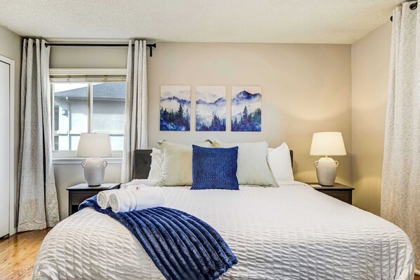 Una habitación de hotel con una cama, dos lámparas de noche, una ventana con cortinas y tres cuadros colgados en la pared.