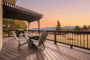 Terraza de madera con pérgola, mobiliario exterior y vista a las montañas.