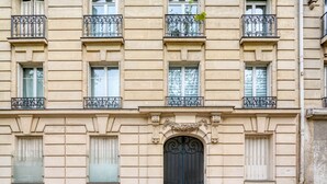A multi-story building with a symmetrical facade, featuring evenly spaced windows with shutters, decorative iron railings on the balconies, and a central ornate door. - Blueground | Porte Saint Cloud, concierge (Paris)