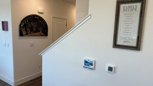 A staircase with a framed family recipe sign, a thermostat, and a small picture frame on the wall. - NEW Smart Home w/ Massage Chair & King Bed (Lathrop)