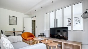 A modern living room with a sofa, orange chair, coffee table, TV, and framed artwork. - Blueground | Montmartre, nr Sacré Coeur (Paris)