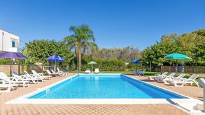 Ein rechteckiger Swimmingpool mit klarem, blauem Wasser, umgeben von weißen Liegestühlen und Sonnenschirmen.