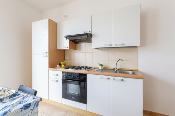A compact kitchen with white cabinets, a black oven, a stainless steel sink, and a wooden countertop.